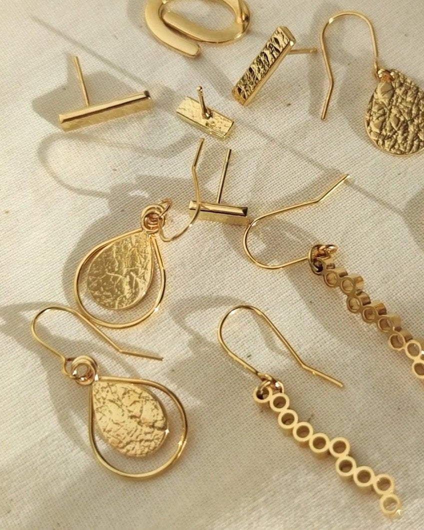 Collection of several handmade gold earrings lying in sunlight on beige fabric