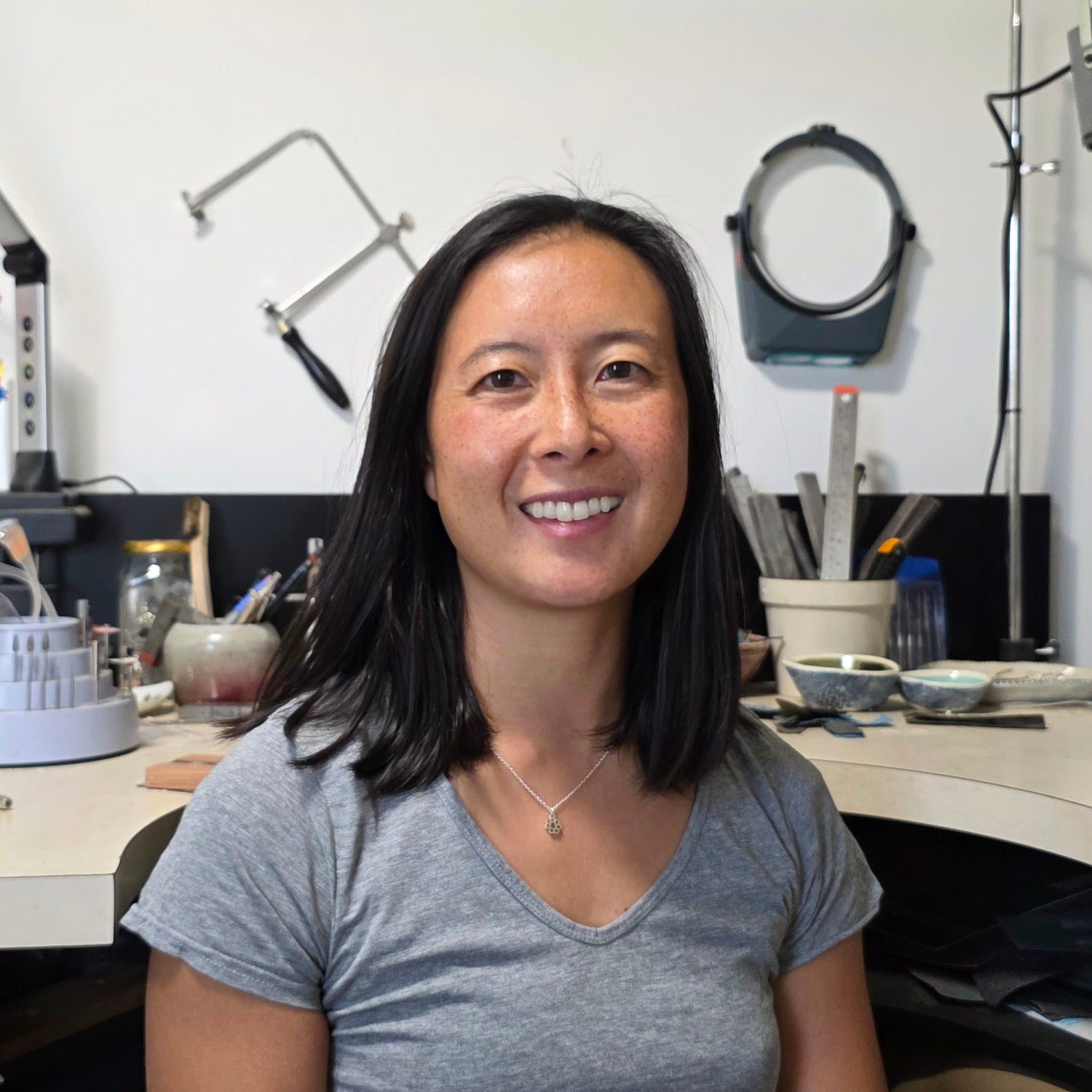 The owner of Aurelium smiling at camera in her jewellery workshop with tools and equipment in the background