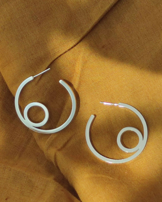 Large sterling silver hoop earrings with circle design lying in shadow on mustard coloured fabric