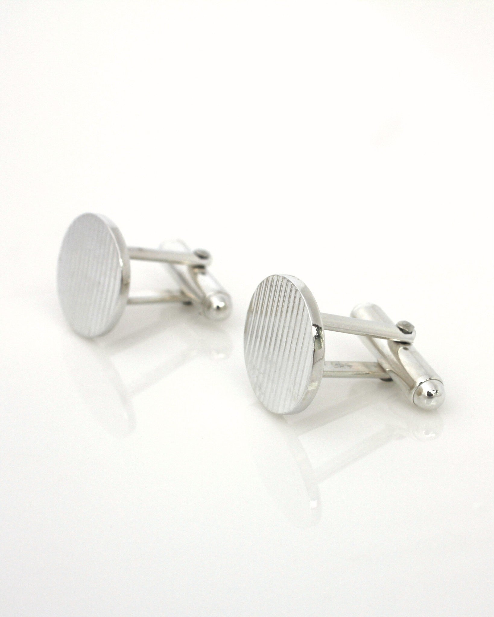 Elegant sterling silver oval cufflinks with ribbon texture lying on reflective white background