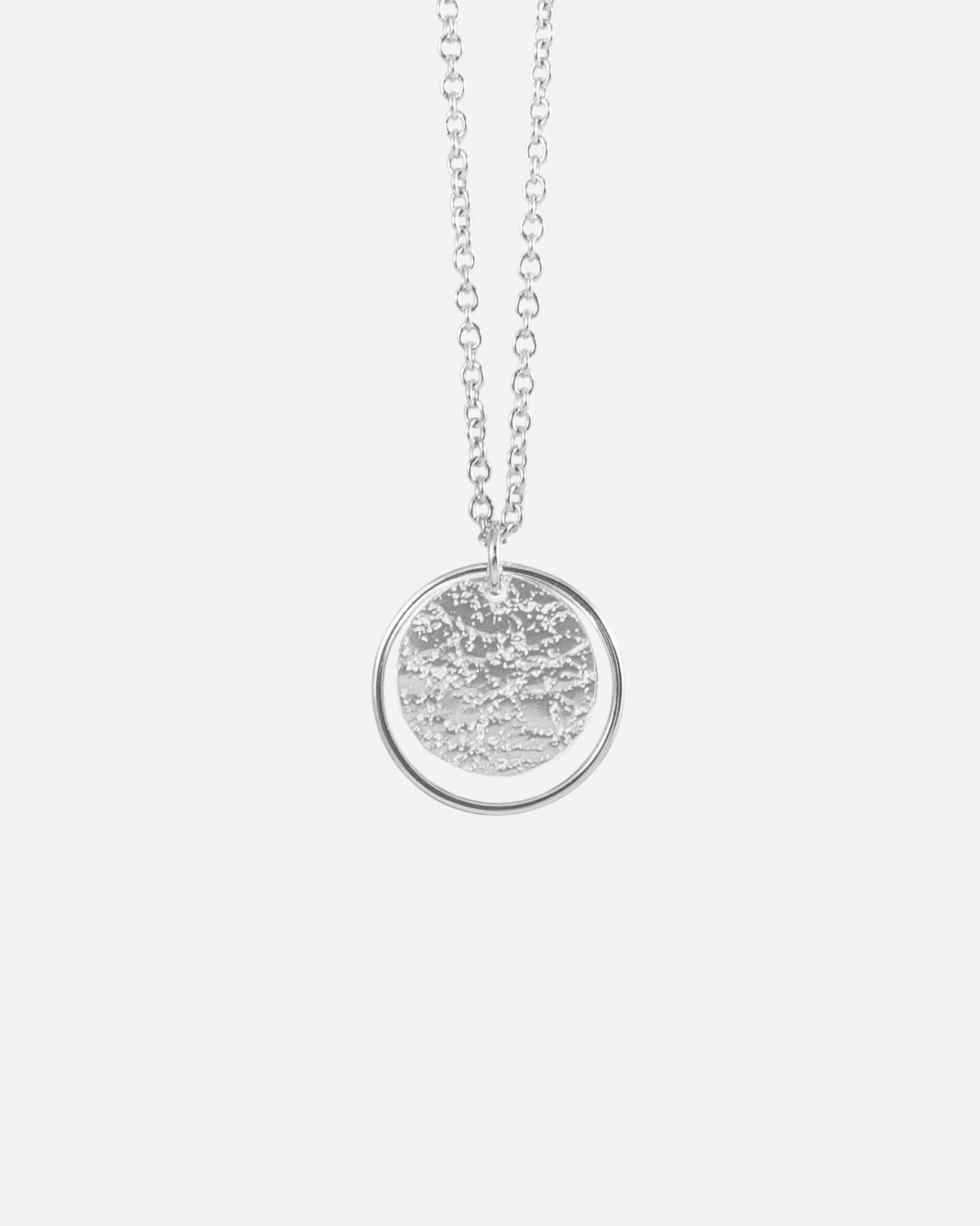 Sterling silver textured circle pendant framed with thin silver loop hanging from fine  cable chain on white background