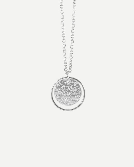 Sterling silver textured circle pendant framed with thin silver loop hanging from fine  cable chain on white background
