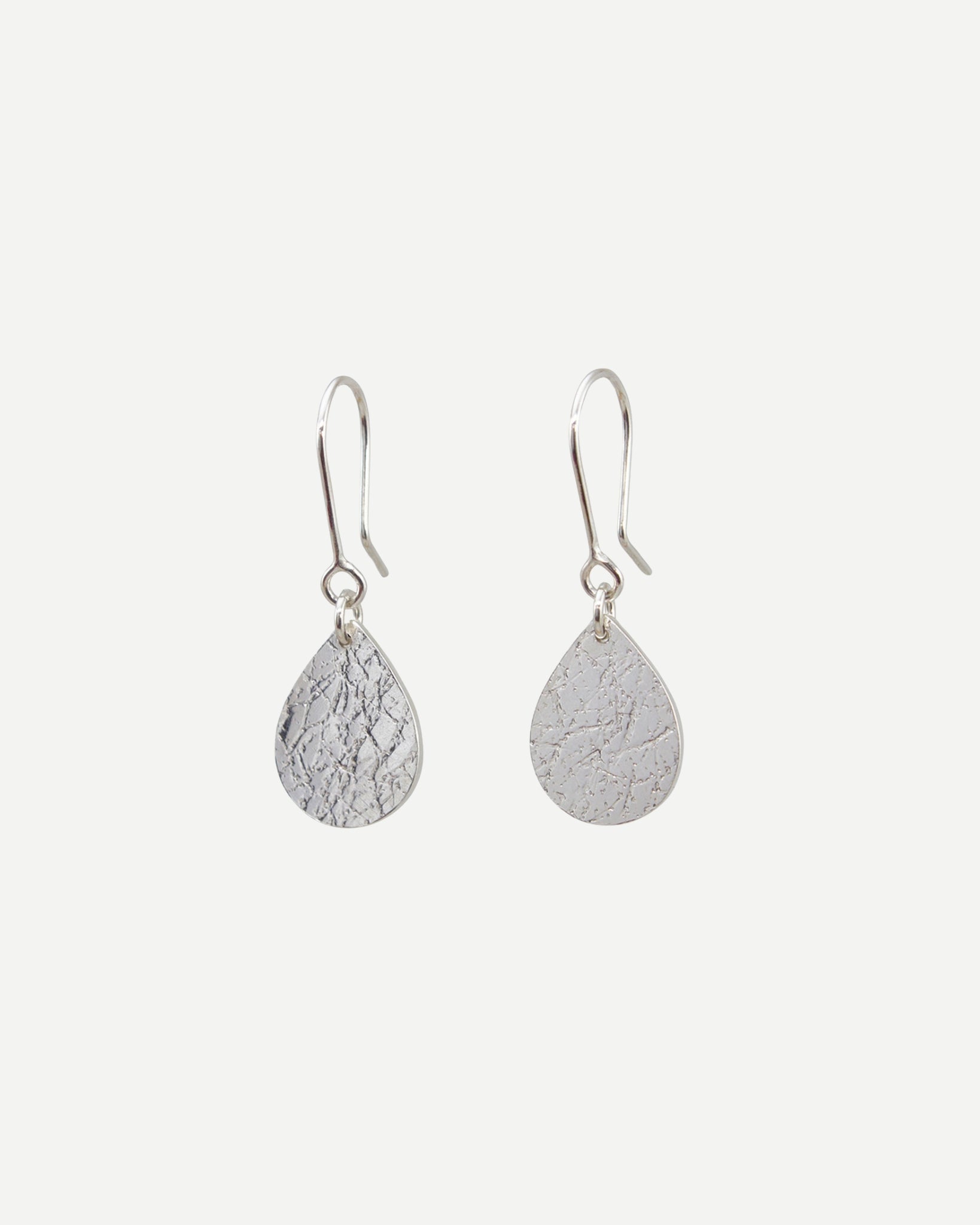 Sterling silver textured teardrop earrings hanging from handmade silver hooks in front of white background