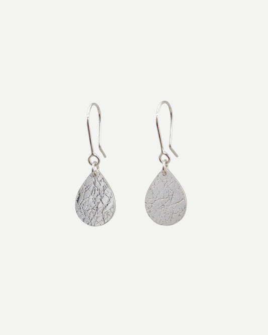 Sterling silver textured teardrop earrings hanging from handmade silver hooks in front of white background