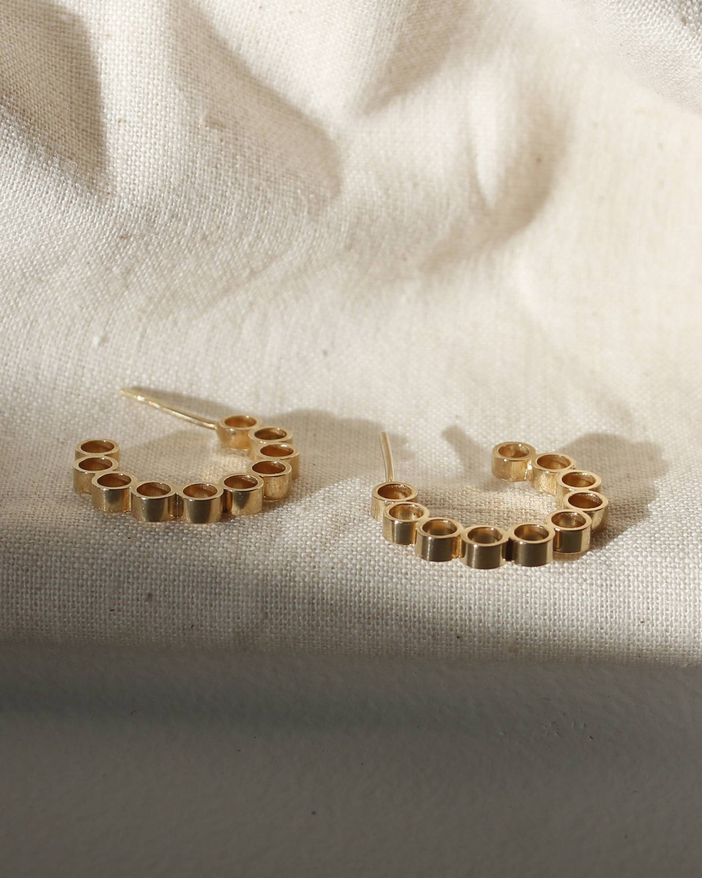 Handmade gold hoop earrings with contemporary circle design lying in sunshine on beige fabric