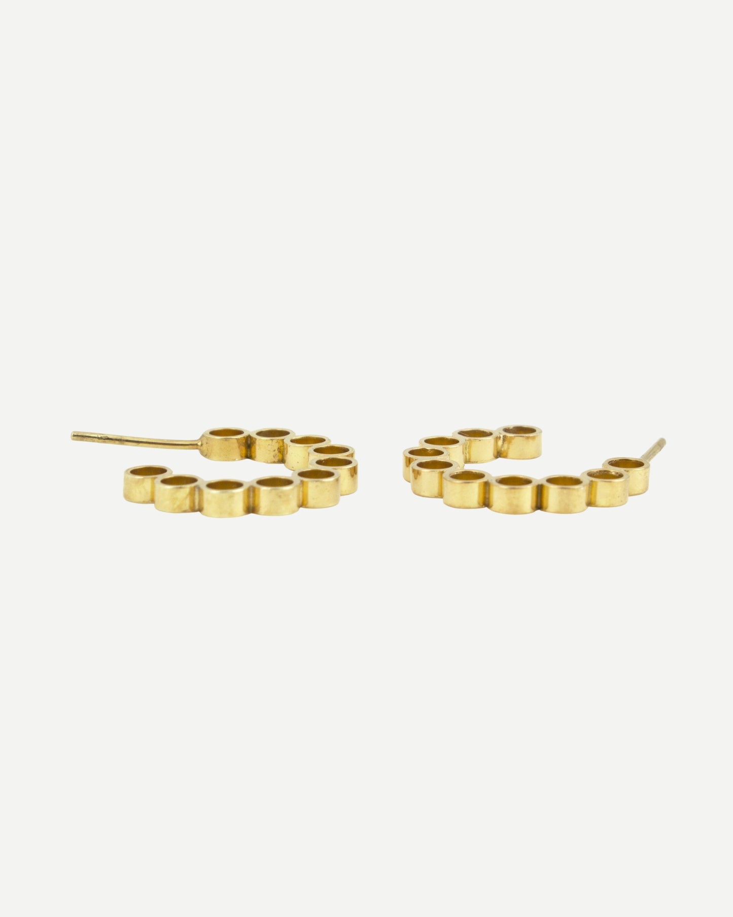Handmade gold hoops earrings with circle design lying on white surface