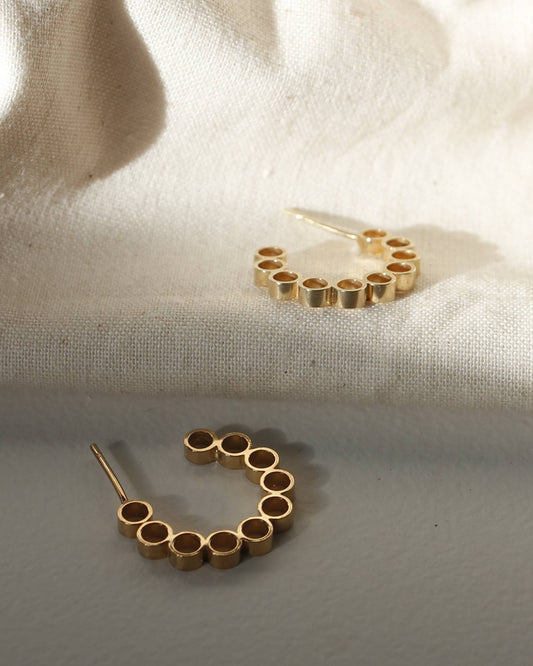 Gold hoop earrings with circle design lying in sunlight on beige fabric