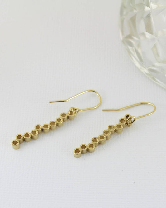 Long dangly gold earrings with circle design lying on white paper