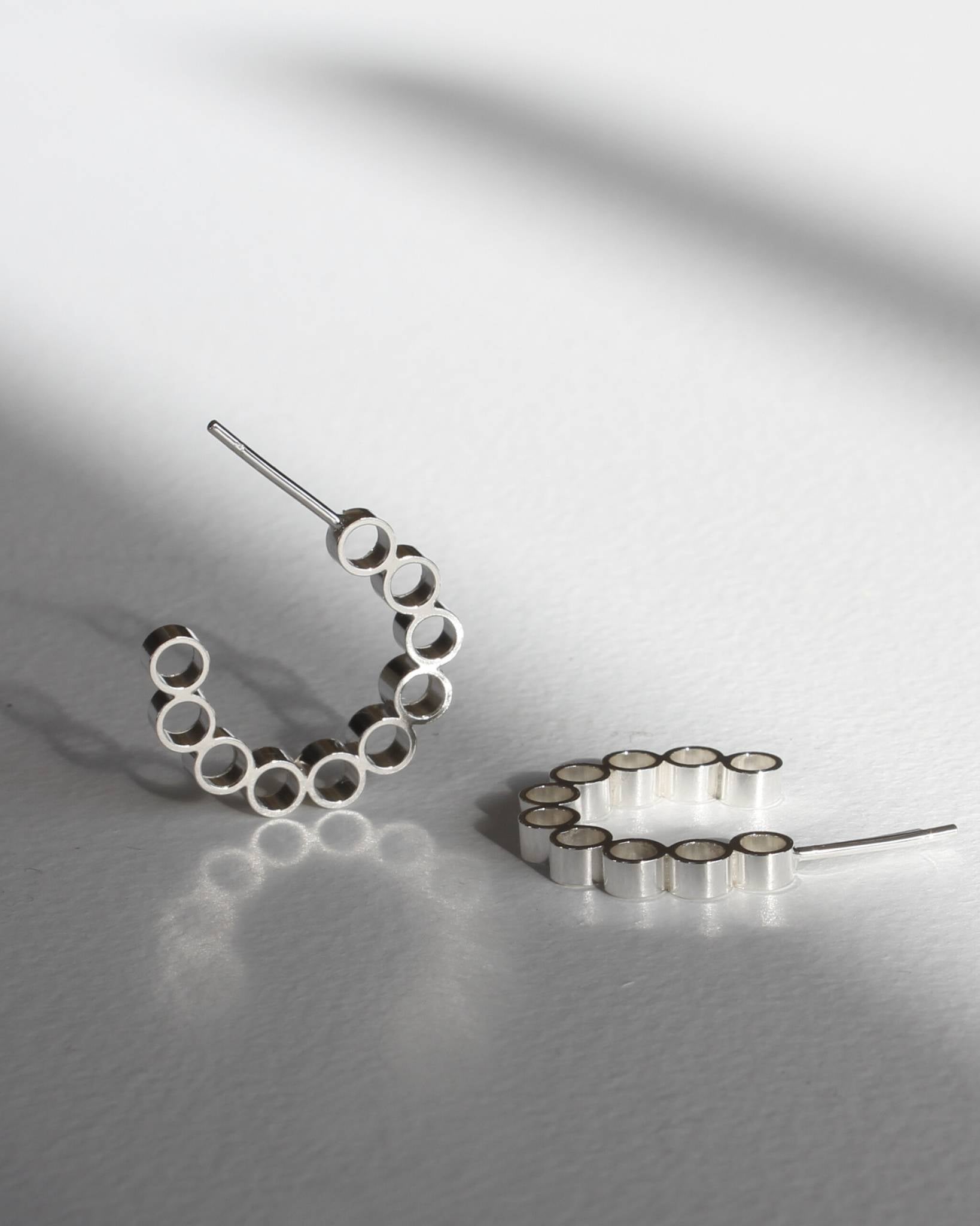 Sterling silver hoop earrings with circle design lying on slightly reflective white surface