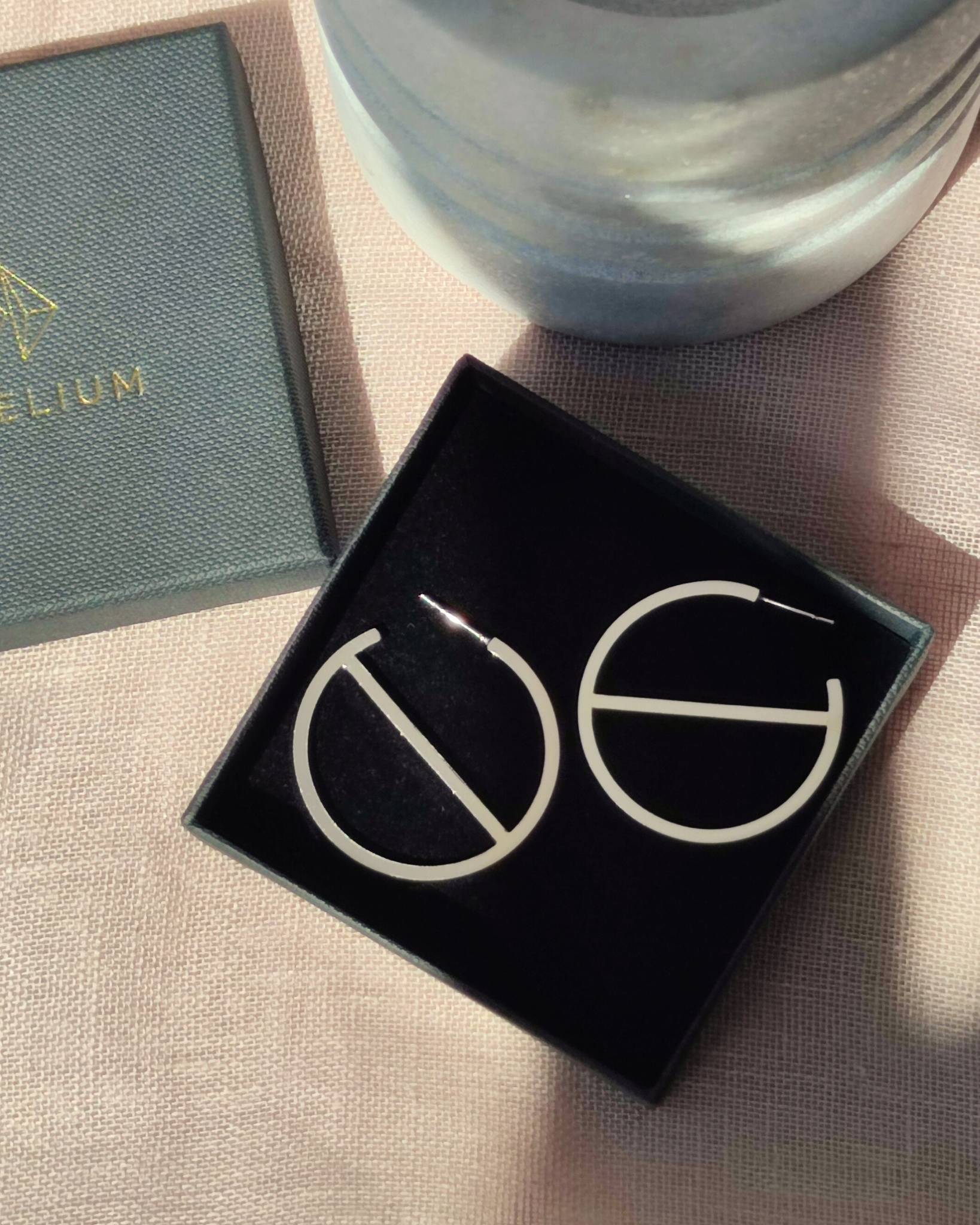 Large sterling silver hoop earrings in minimalist design lying in black gift box in partial sunlight