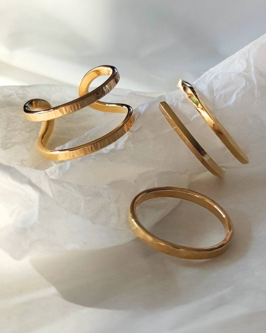 Three dainty gold minimalist rings lying on crumpled white tissue paper