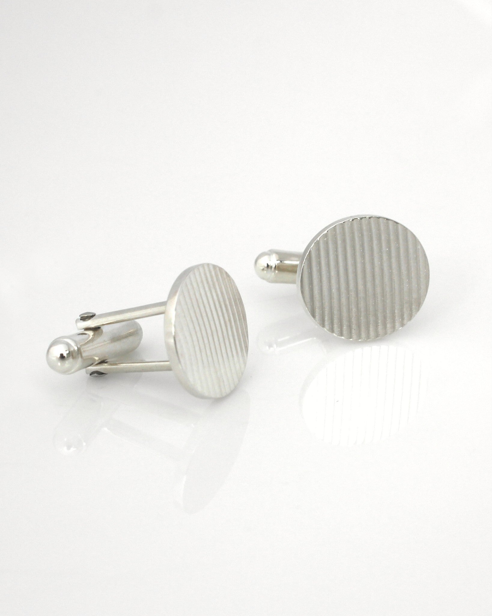 Silver oval cufflinks with ribbon texture on reflective white background