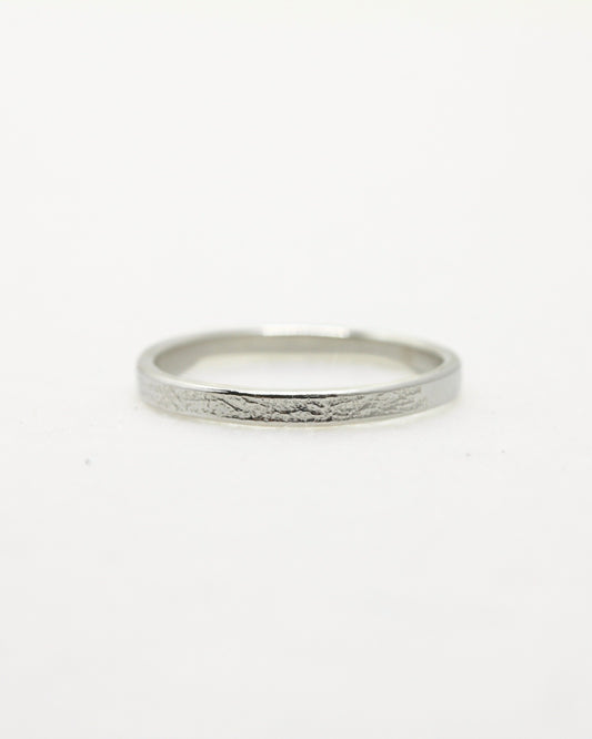 Dainty sterling silver stacking ring with delicate texture lying on white surface