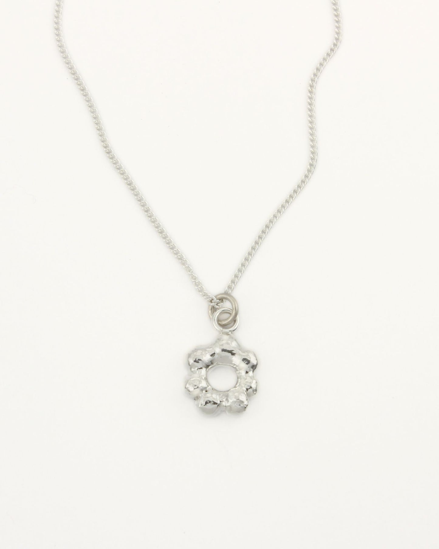 Small flower-shaped molten silver pendant attached to fine silver curb chain on white background