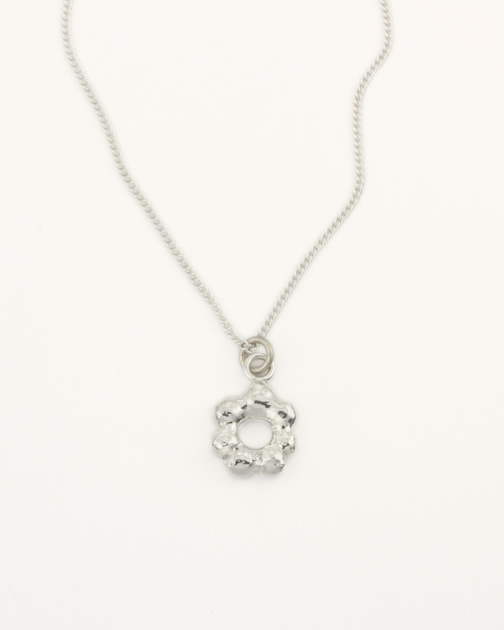 Small flower-shaped molten silver pendant attached to fine silver curb chain on white background