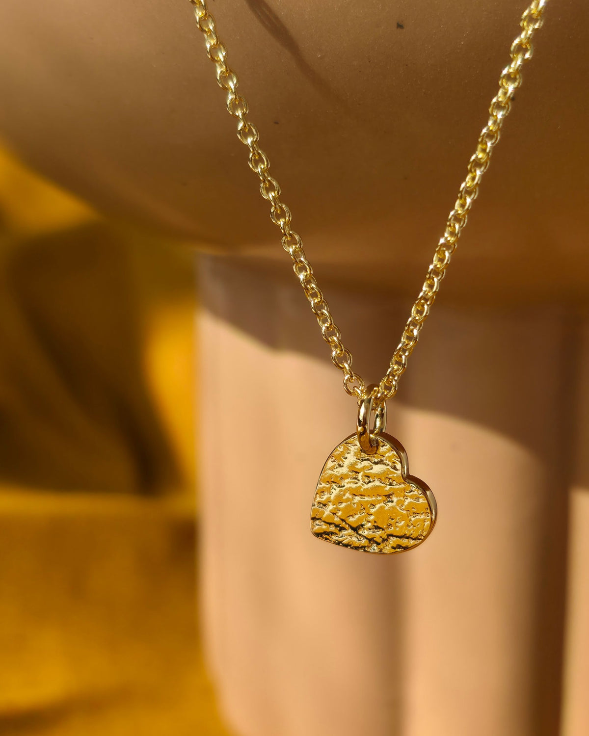 Gold necklace with a textured heart pendant on a neutral background