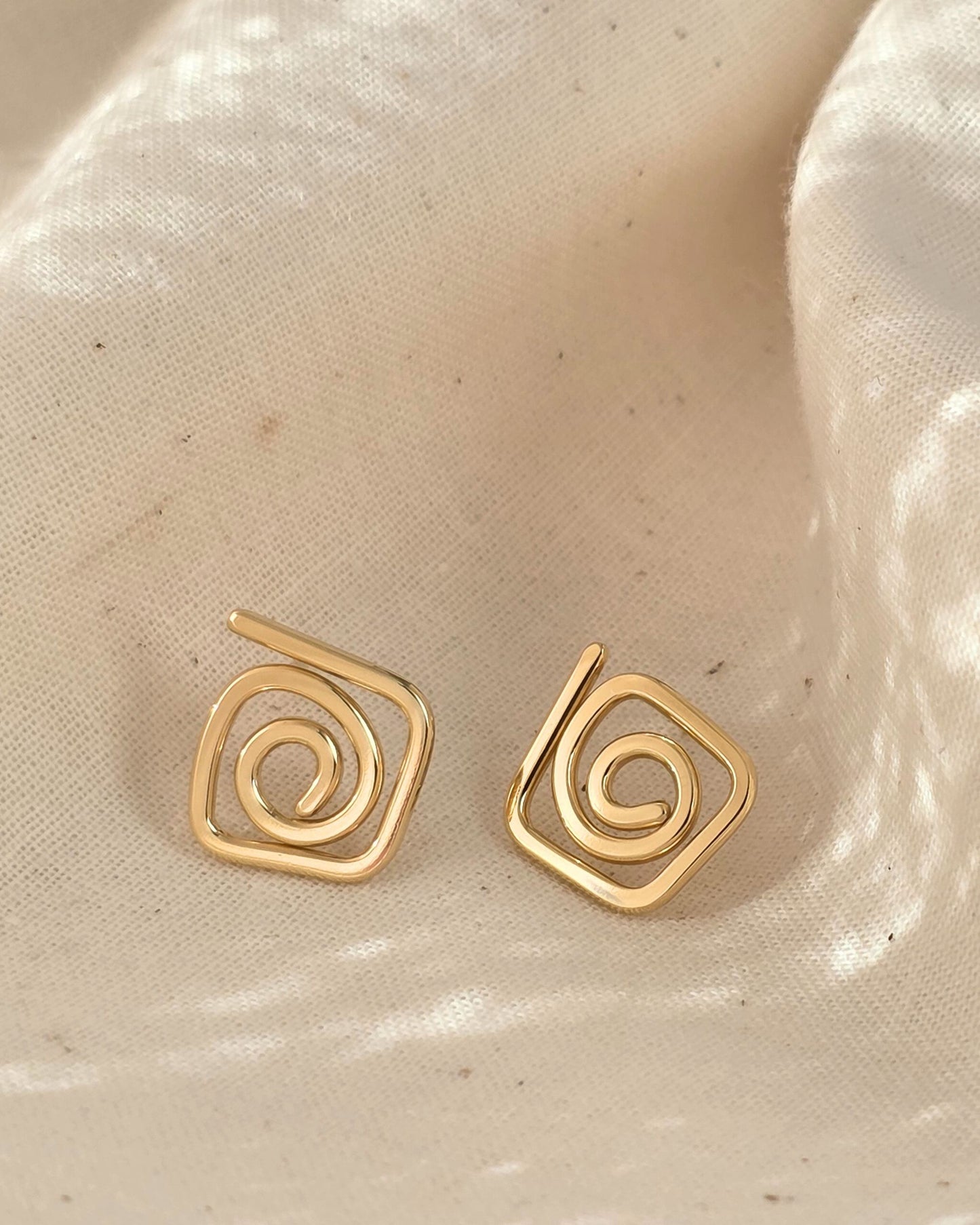 elegant gold diamond swirl spiral studs on cream textured background