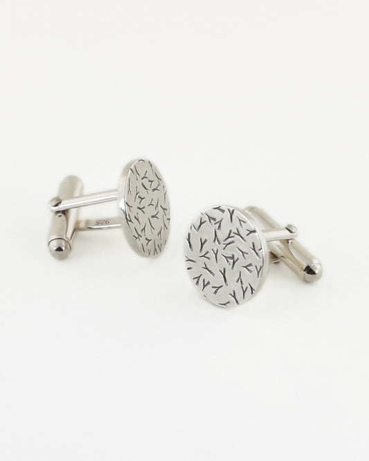 Front and side views of silver circle-shaped cufflinks with a contrasted silver and black textured surface, with white background