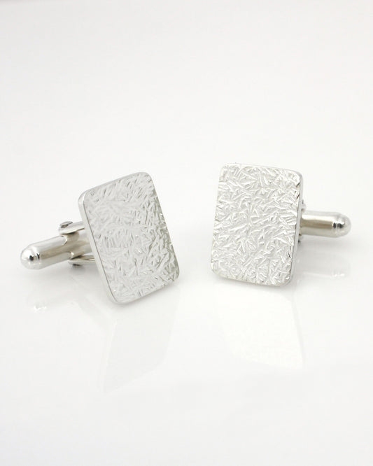 Silver rectangle cufflinks with textured surface, lying on white background