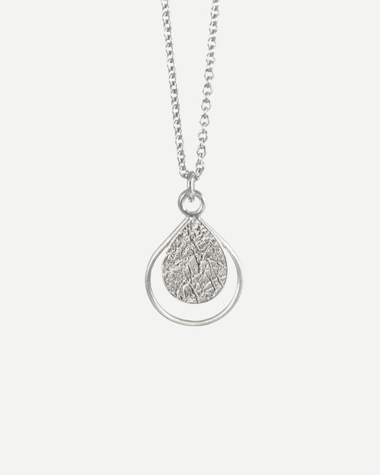 Delicate textured silver teardrop within thin silver teardrop-shaped wire hanging from fine silver chain, on white background