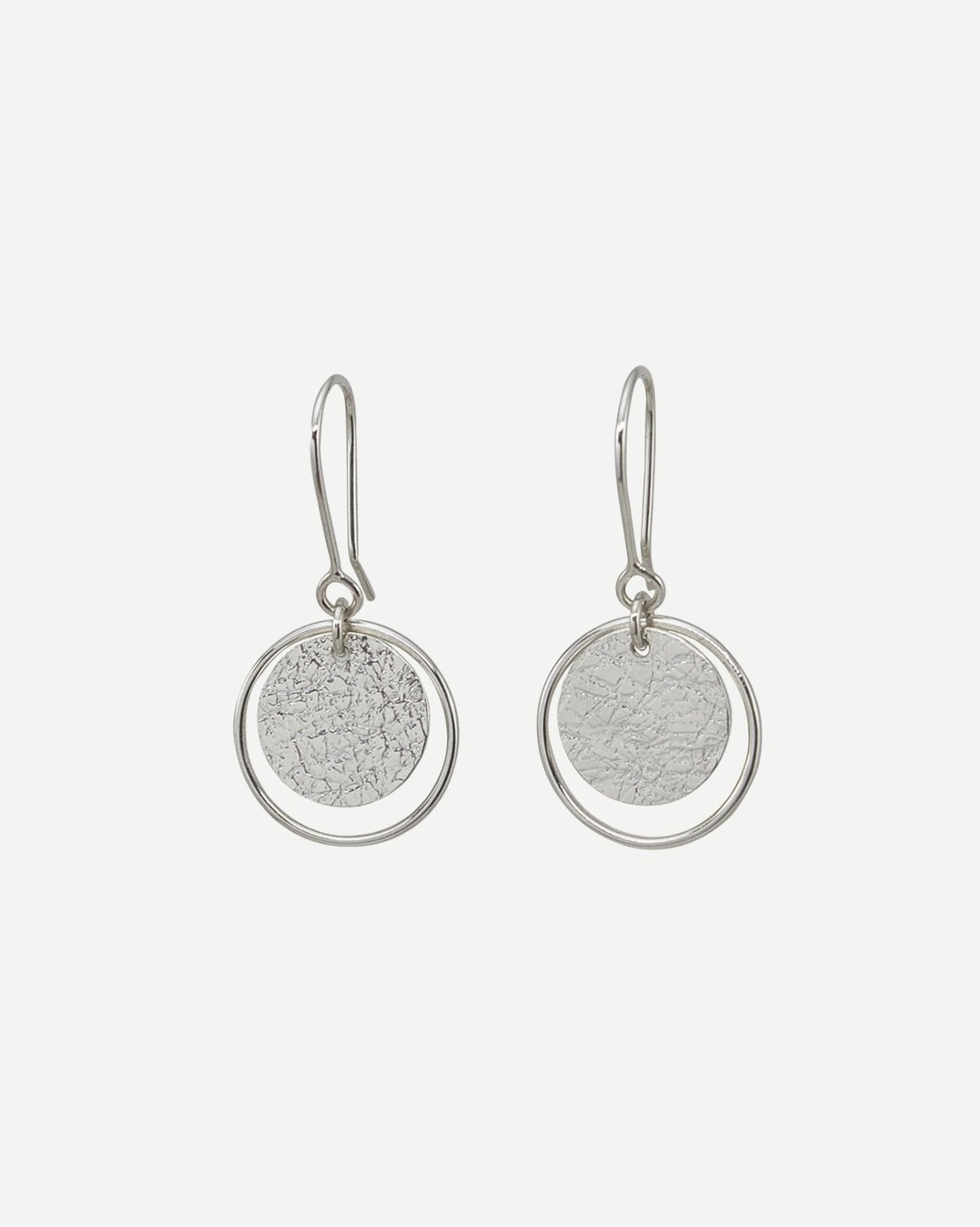 Earrings consisting of textured silver circles within thin silver loops hanging on handmade silver hooks on white background