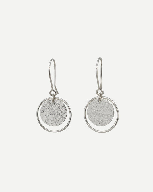 Earrings consisting of textured silver circles within thin silver loops hanging on handmade silver hooks on white background