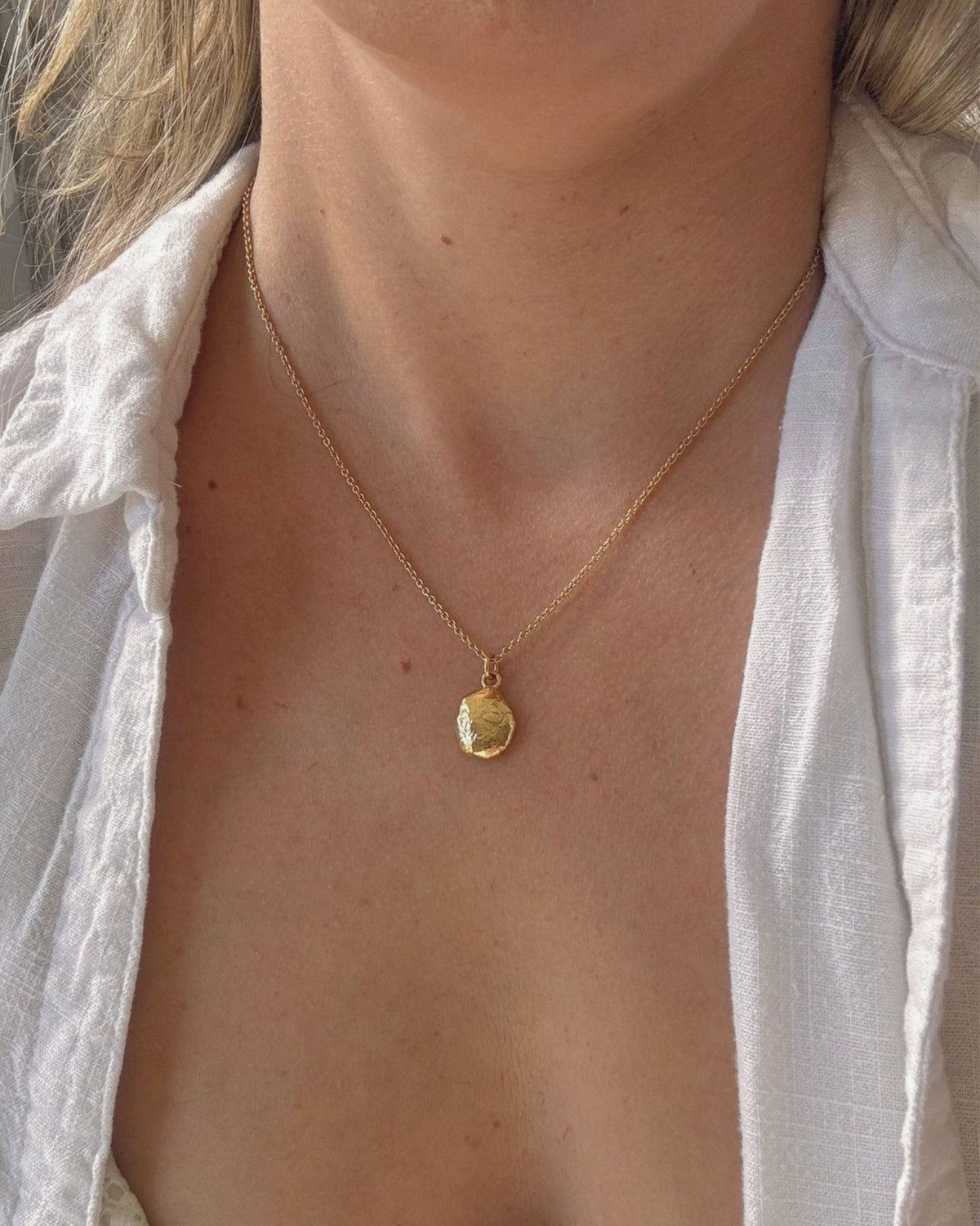Person in a white shirt wearing a necklace with a small gold oval pendant
