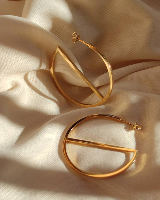 Large gold hoop earrings in minimalist design lying in sunlight on soft beige fabric