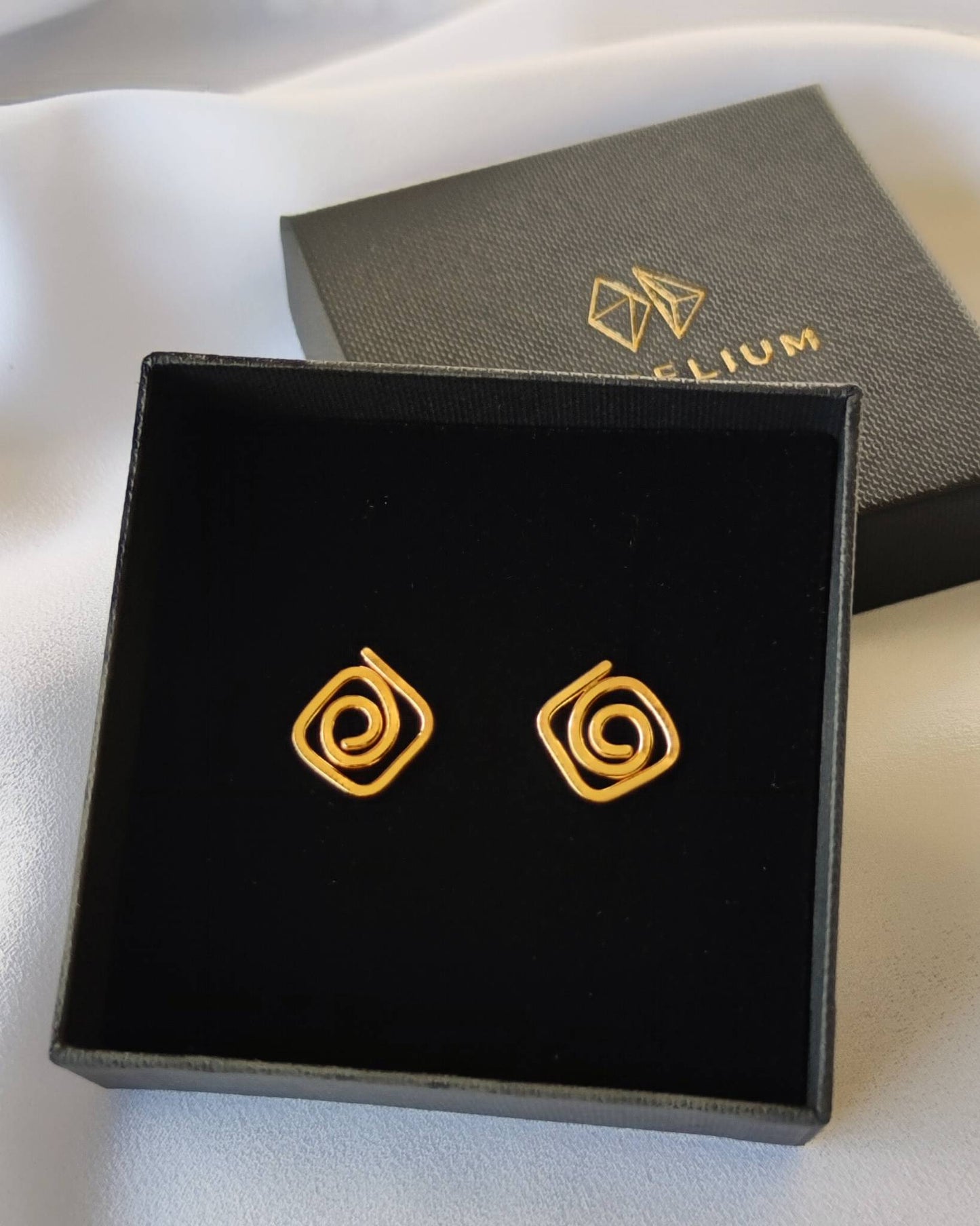 Small gold diamond-shaped stud earrings in swirl design presented in black jewellery gift box