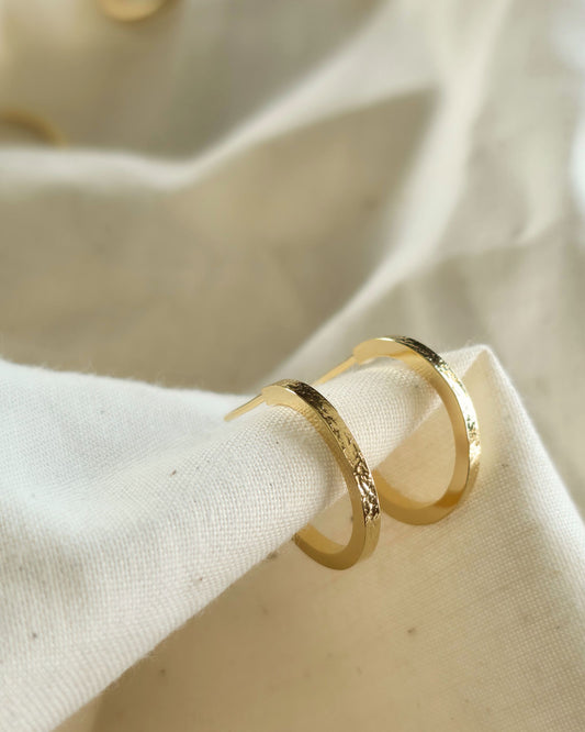 Small gold textured hoop earrings on a beige fabric background