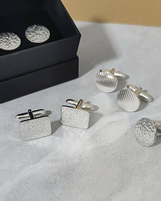 Collection of four pairs of sterling silver cufflinks in geometric shapes with textured surfaces lying on marbled paper