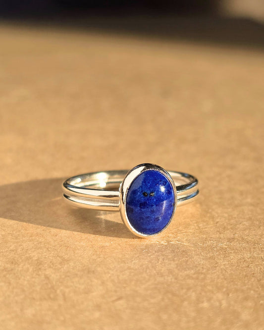 Handmade sterling silver ring set with a deep blue lapis lazuli cabochon stone lying on brown paper