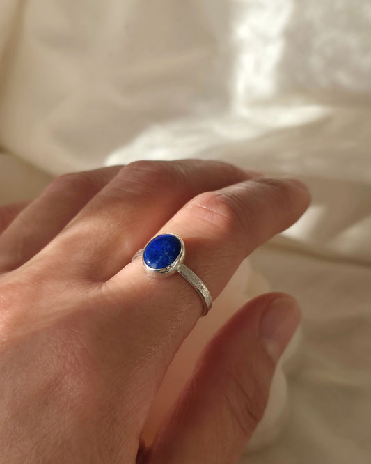 Hand wearing a silver ring with a vivid blue lapis lazuli stone on a light background