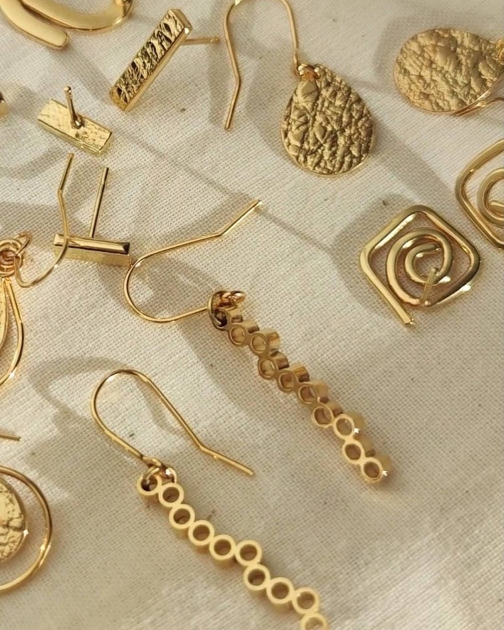 Collection of textured gold earrings lying on beige fabric