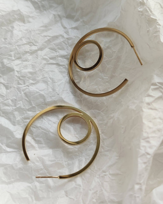 Large gold hoop earrings in minimalist style lying on crumpled white tissue paper