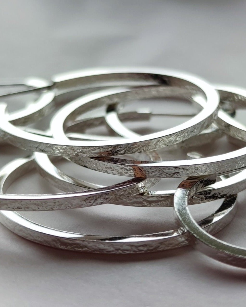 Pile of small and large textured sterling silver hoop earrings lying on grey surface
