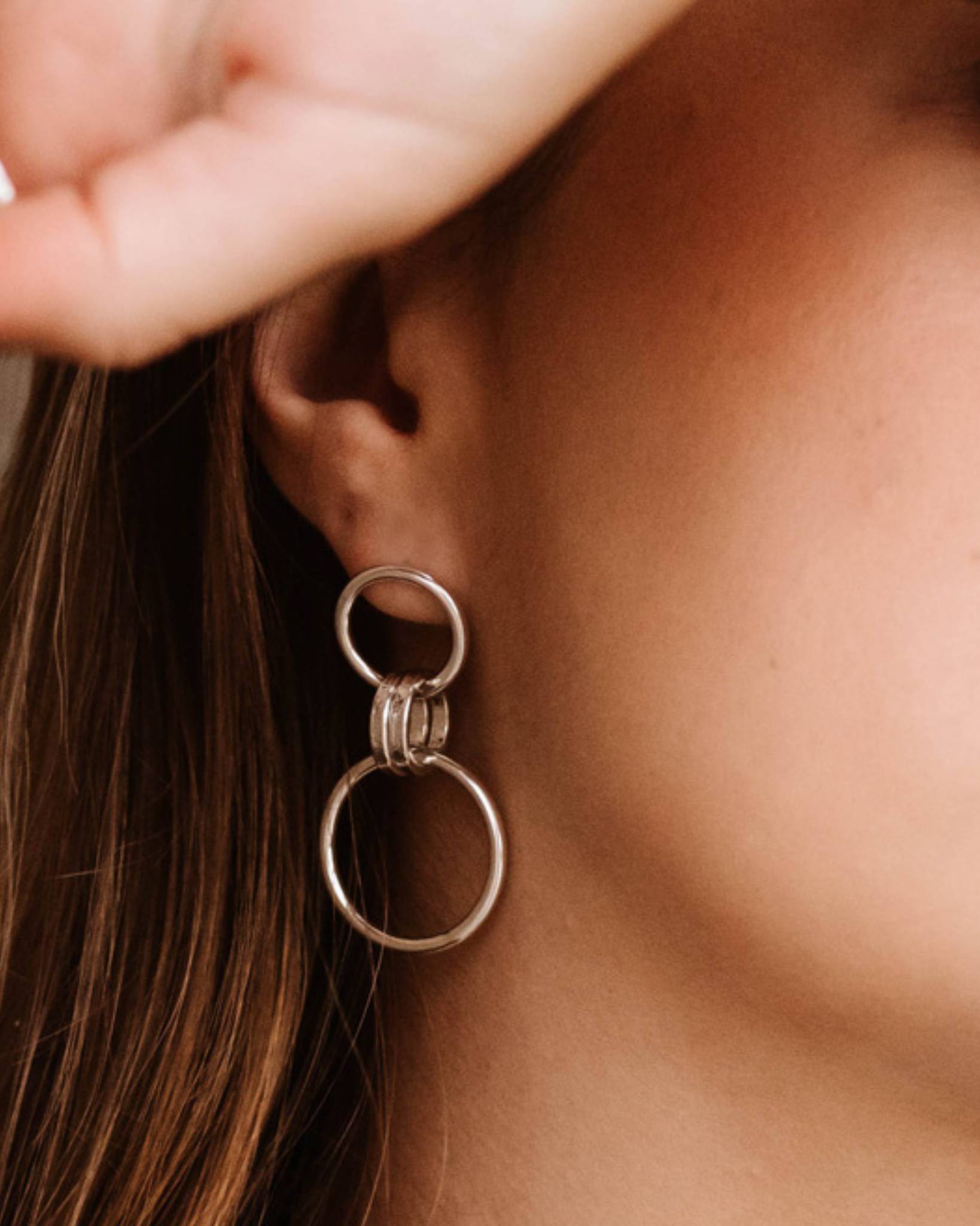 Close up of person wearing minimalist sterling silver drop earrings with small and large loops