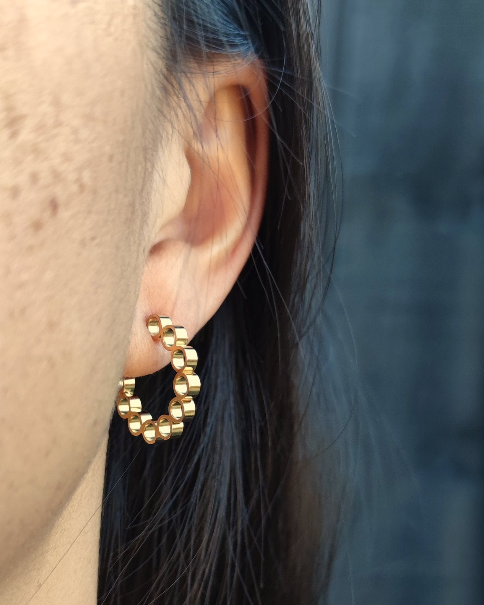 Front view of person with black hair wearing gold hoop earrings made from multiple small circular tube