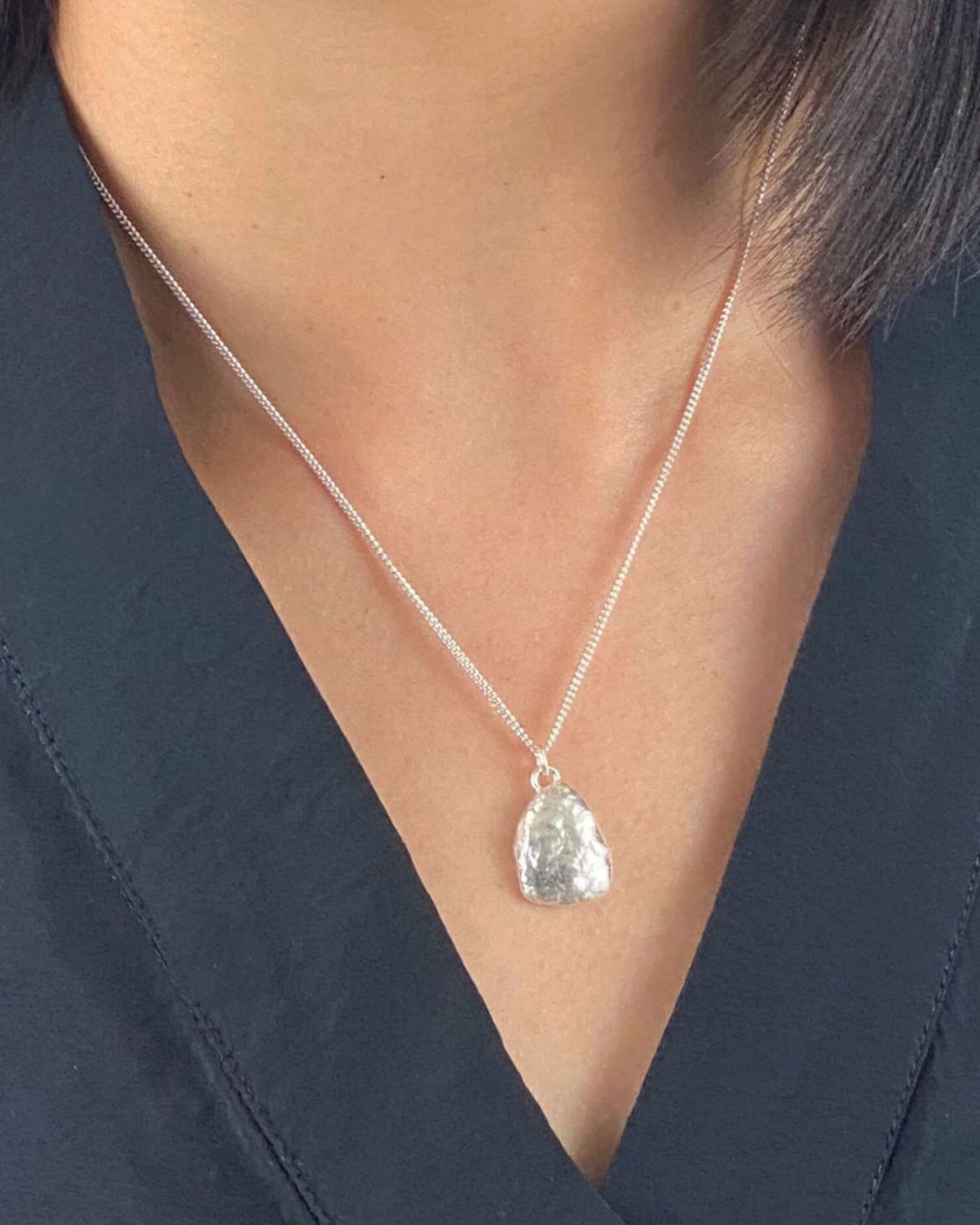Person wearing triangle-shaped molten silver pendant hanging from fine silver chain