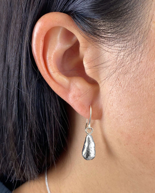 Person wearing long dangly teardrop-shaped molten silver earrings on handmade hooks