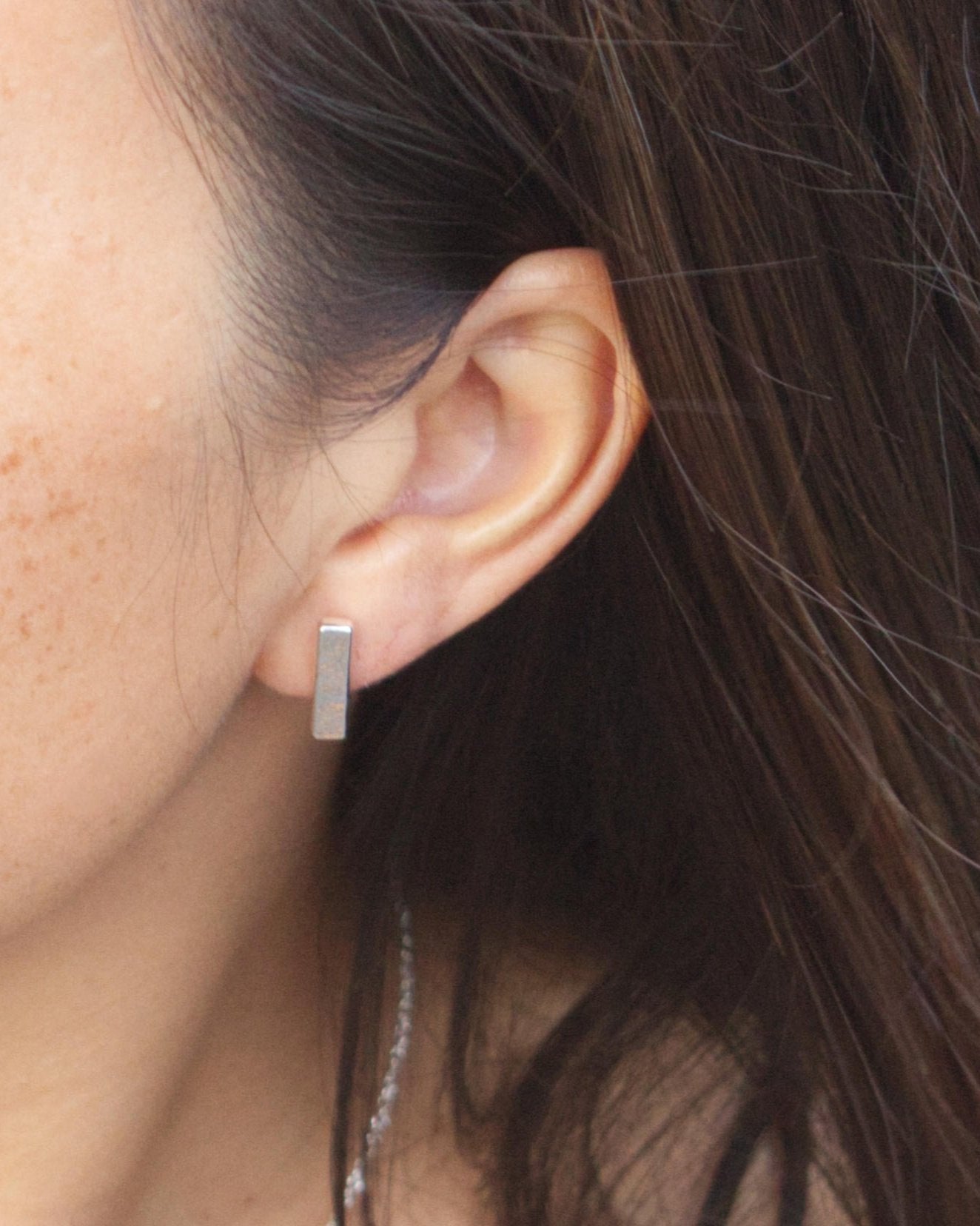 Person wearing long silver rectangle bar stud earrings