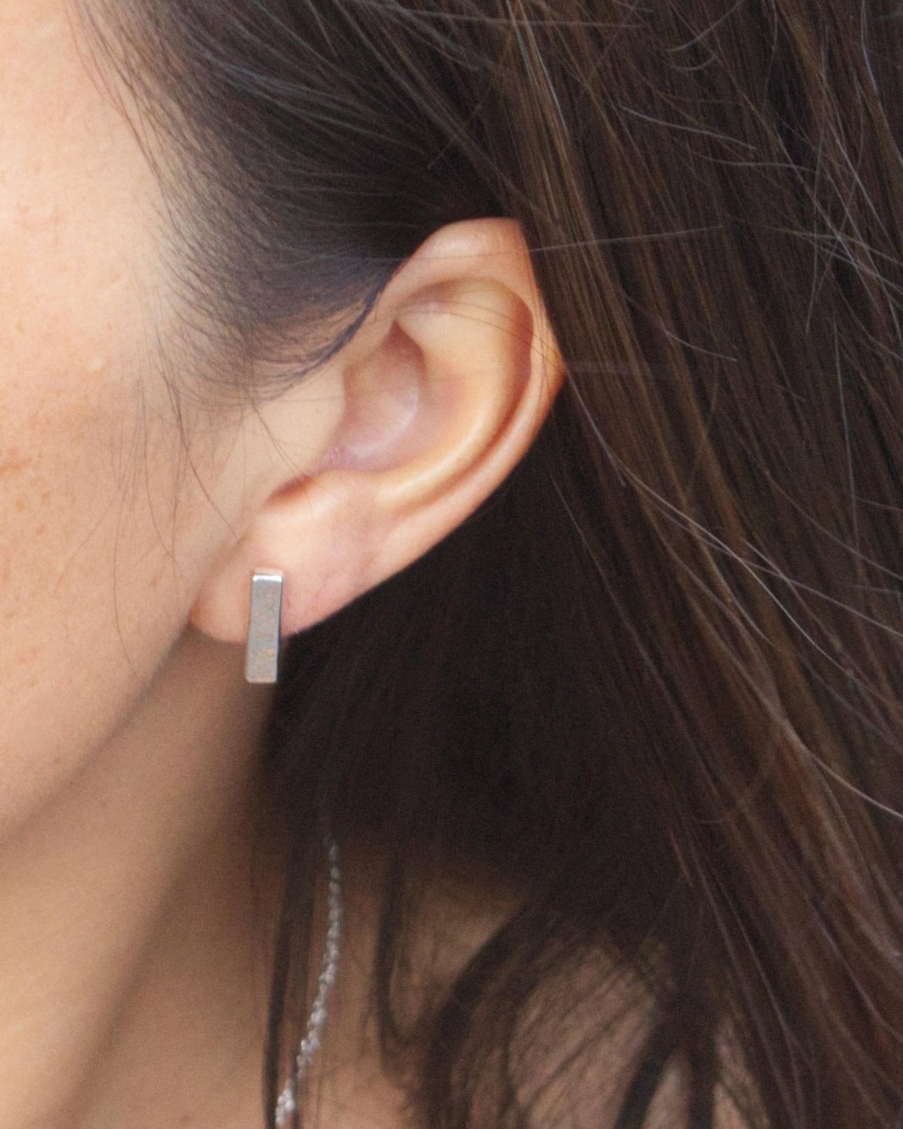 model wearing minimalist silver bar stud earrings with textured detail