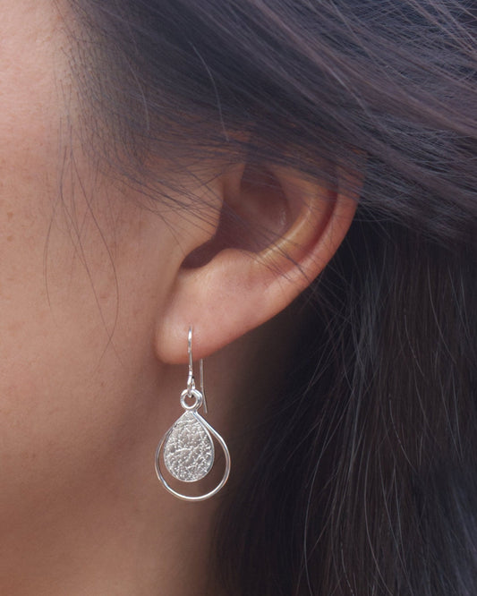 Person wearing dainty sterling silver teardrop-shaped earrings with textured surface