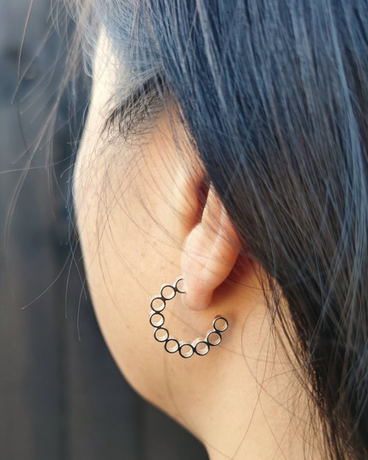 Side view of person with black hair wearing silver hoop earrings made from multiple small circles