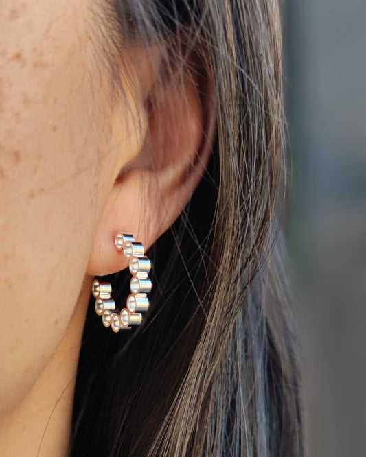 Front view of person with black hair wearing silver hoop earrings made from multiple small circles