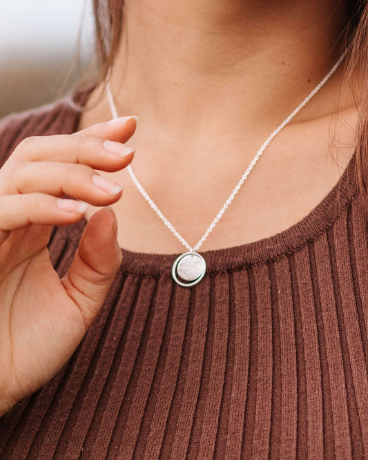 Person in brown top wearing textured silver circle pendant framed by a thin silver wire loop