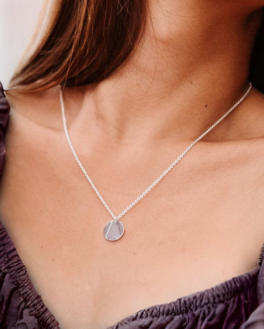 Person wearing silver circle pendant with partially textured surface in triangle shape, hanging on fine silver chain