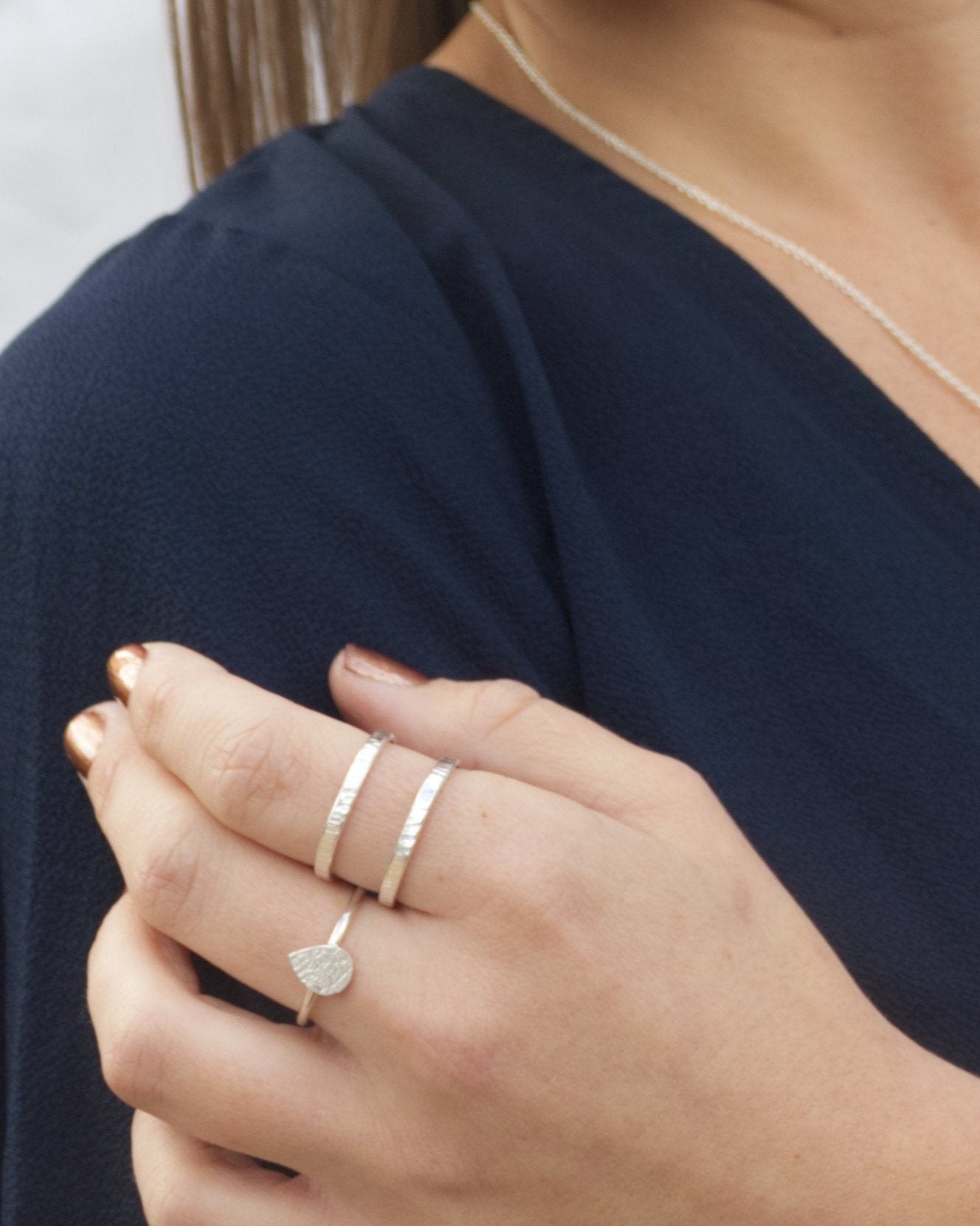 Person in dark blue top wearing silver double band ring and teardrop ring with hand on upper arm