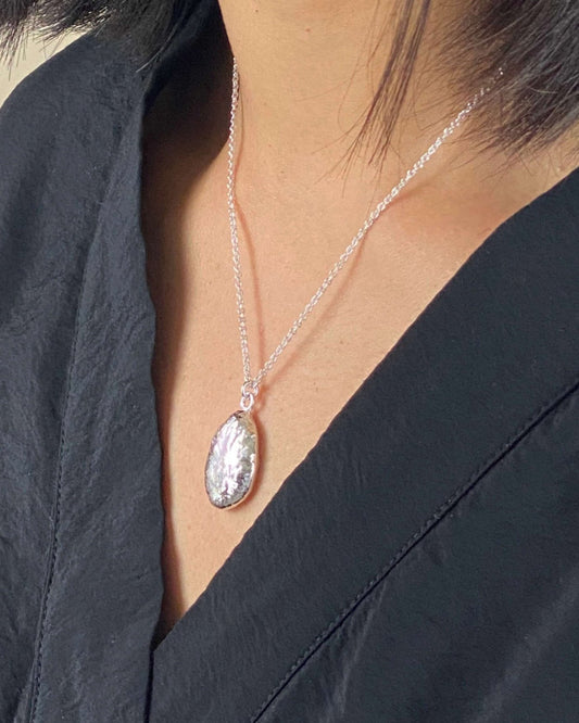 Person wearing oval shaped molten silver pendant with reflective rippled texture hanging on fine silver chain