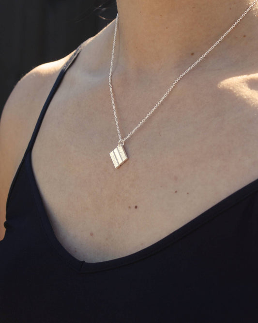 Person wearing silver square pendant with partially textured surface hanging on fine silver chain